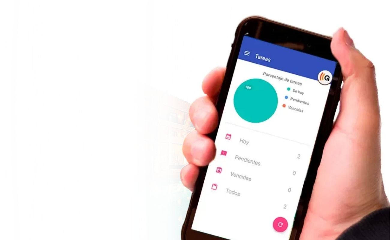 Mano sosteniendo un radio comunicador que muestra un panel de control con el porcentaje y estatus de tareas para la gestión de un hotel, con el fondo borroso de un hotel y su piscina.