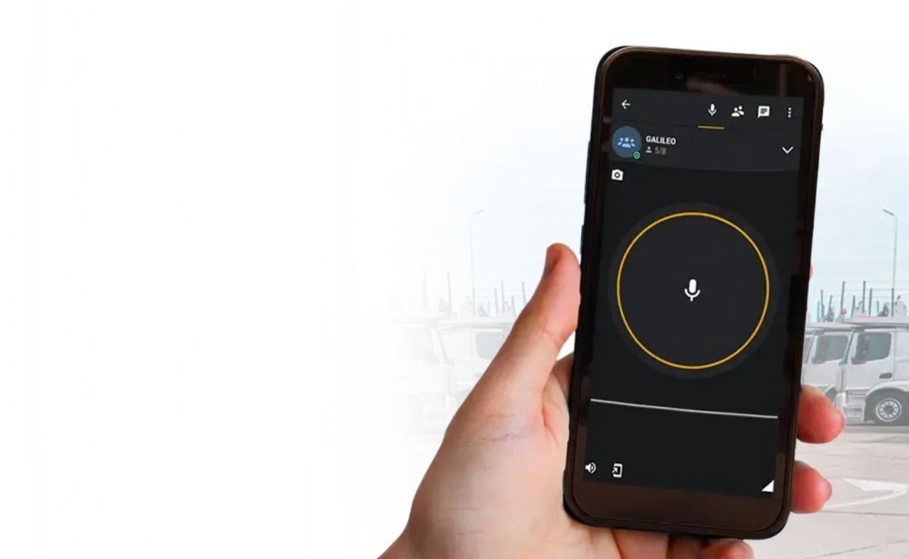 Mano sosteniendo una radio PTT de Galileo con la pantalla encendida mostrando la aplicación de geolocalización de una flota de camiones.