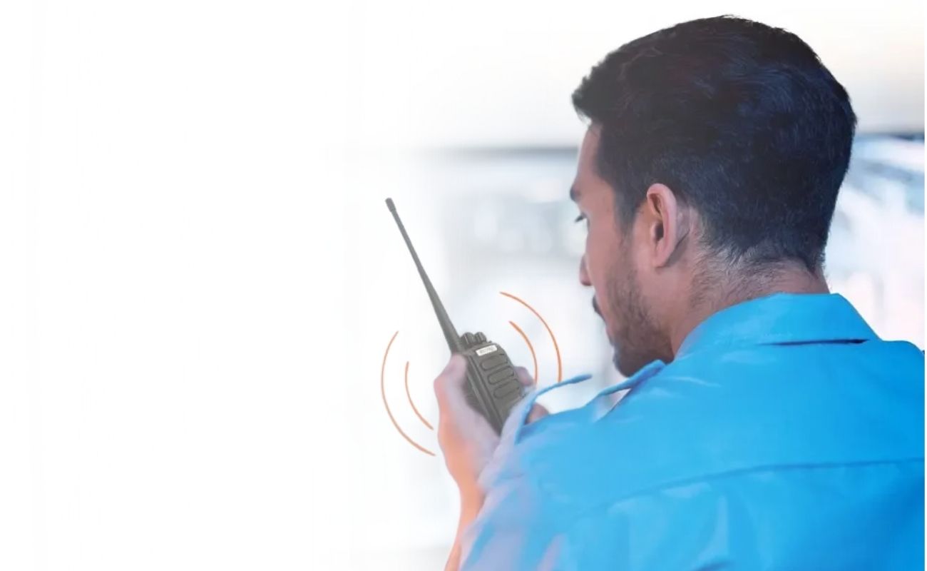 Mano sosteniendo un radio PoC con una aplicación de gestión de asistencias, mostrando el registro de un guardia de seguridad privada con el logo de Galileo.