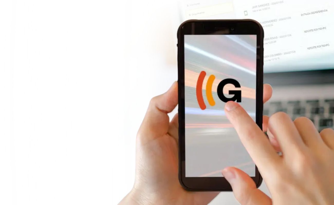 Mano de una persona tocando la pantalla de un smartphone que muestra el logo de Galileo, con una laptop de fondo que muestra una plataforma de gestión de información.