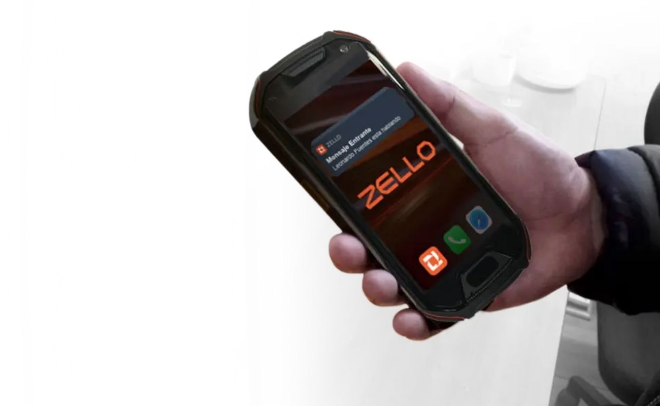Mano sosteniendo un smartphone de uso rudo mostrando la aplicación de Zello, con un mensaje entrante que notifica la ubicación de un usuario.