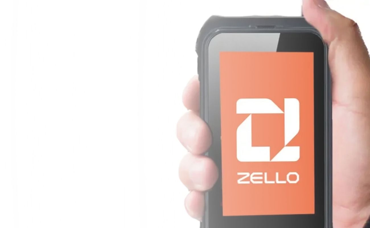 Mano sosteniendo un smartphone de uso rudo con el logo de la aplicación Zello en pantalla, representando la radiocomunicación moderna.