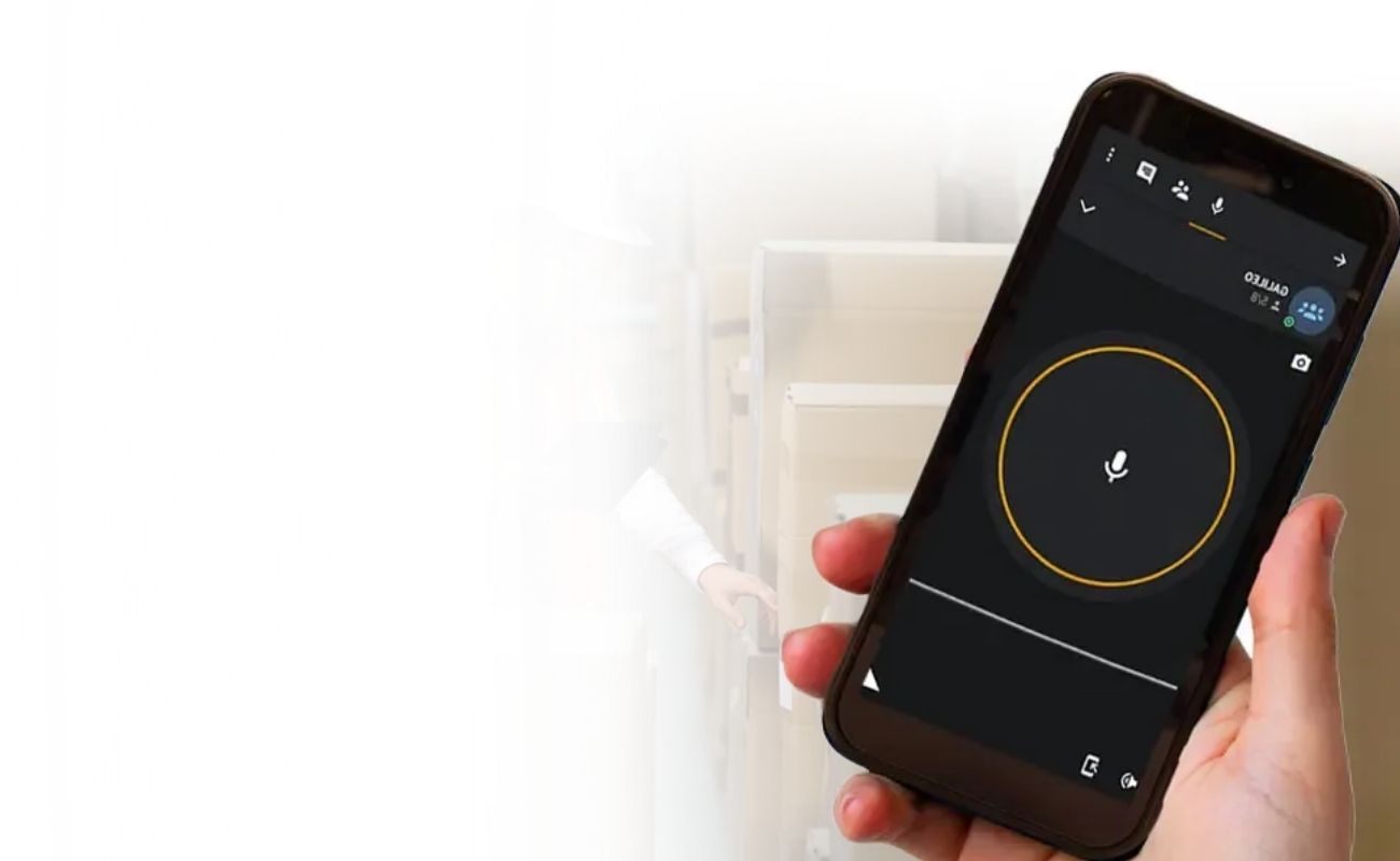 Mano sosteniendo un smartphone con una aplicación de radiocomunicación PTT y geolocalización, con un trabajador de almacén de fondo.