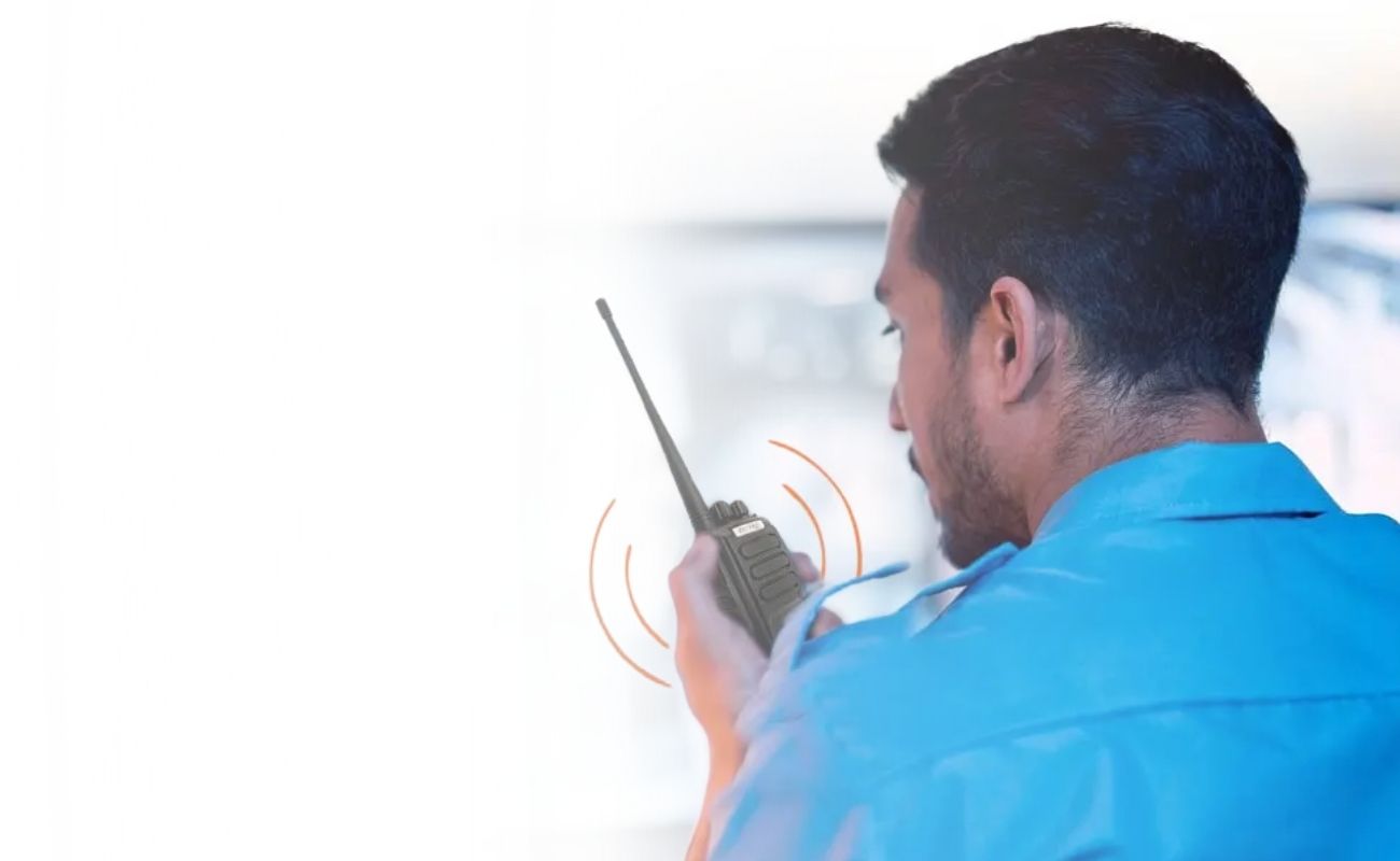 Guardia de seguridad privado usando un radio de radiocomunicación, con un centro de monitoreo de cámaras de vigilancia de fondo.