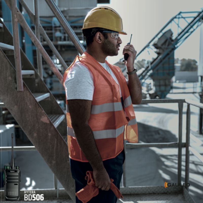 Trabajador con casco, lentes y chaleco de protección hablando por un radiocomunicador de galileo, modelo hytera BD506