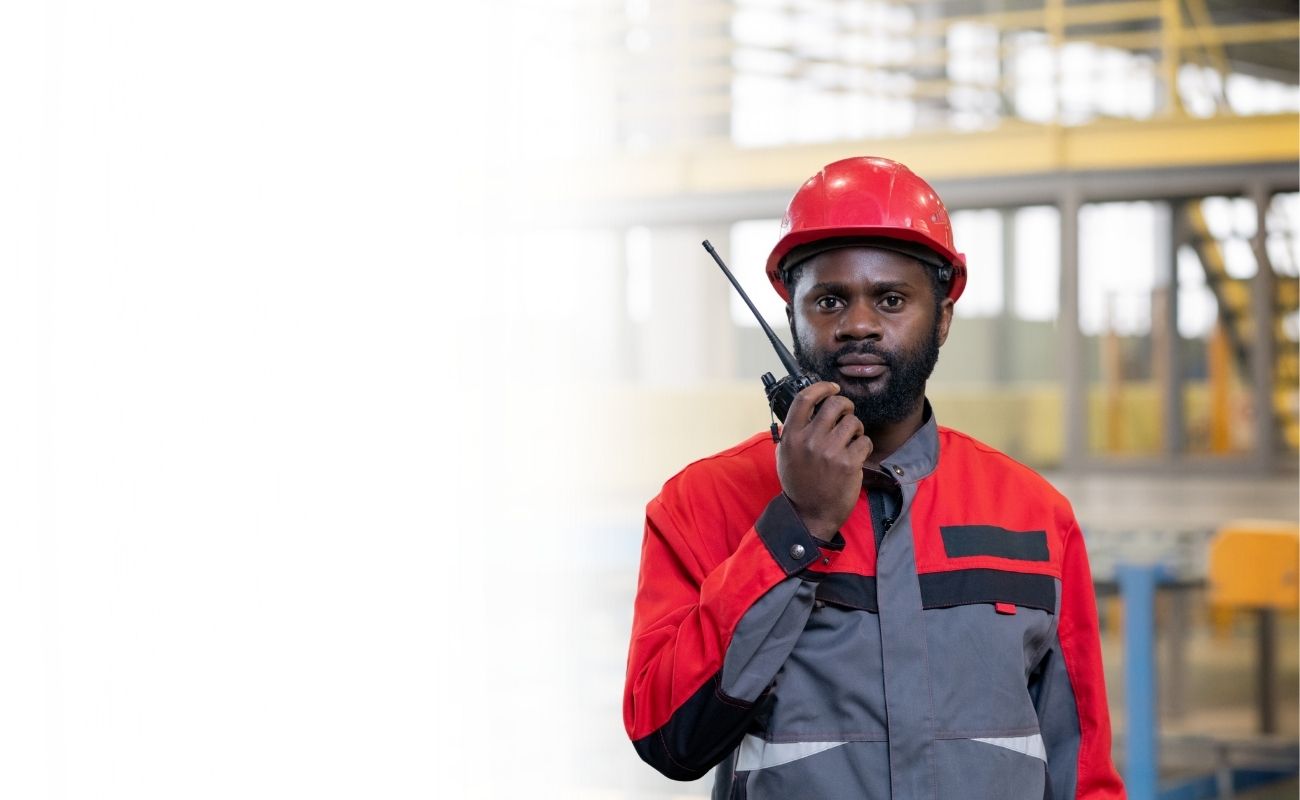 Operario industrial utilizando un radio PoC con Zello Work para comunicación instantánea en una planta de producción.