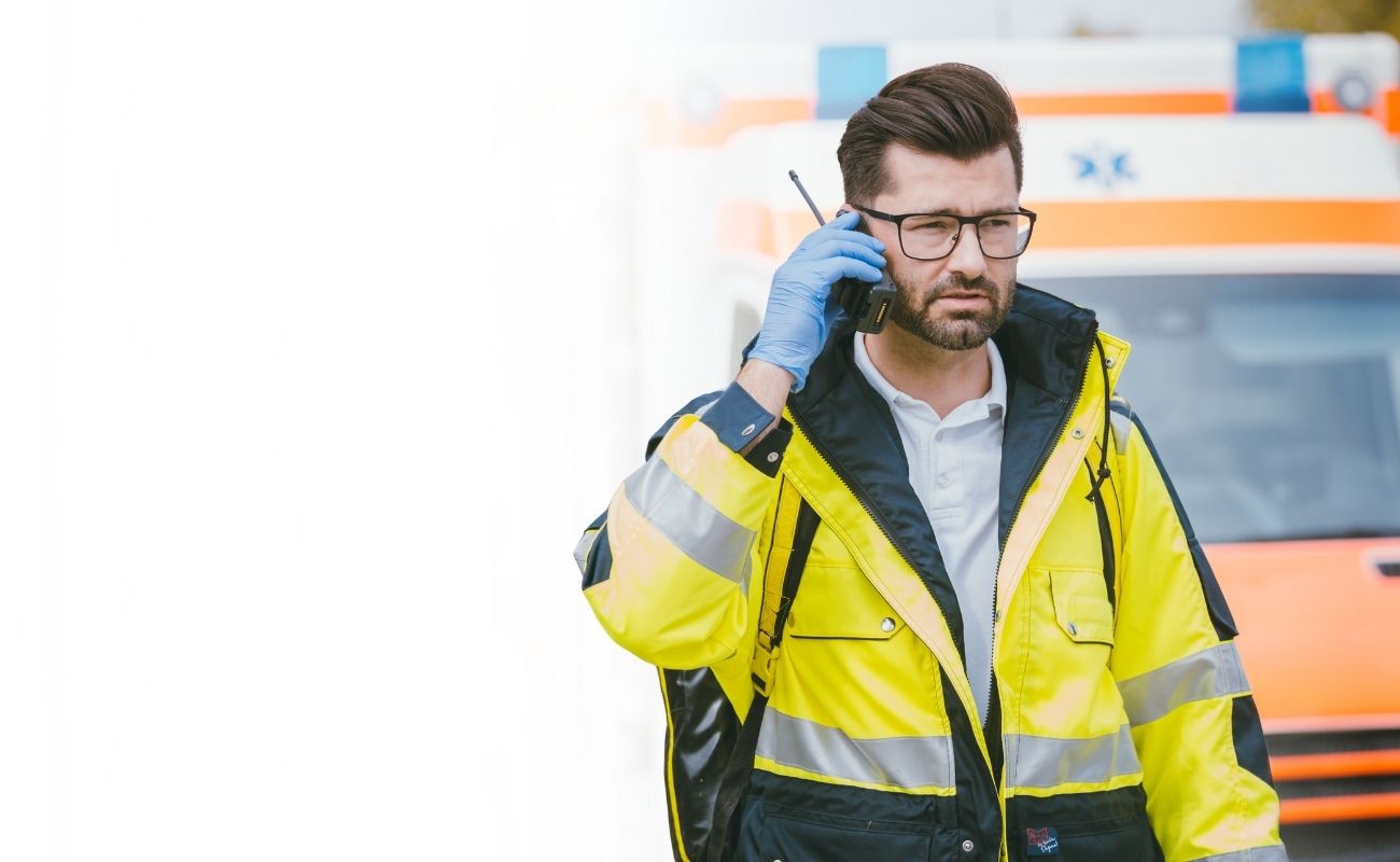 Paramédico utilizando un radio PoC con inteligencia artificial frente a una ambulancia para coordinar una respuesta de emergencia.
